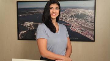 servidora posa na frente de quadro com foto da Cidade #paratodosverem