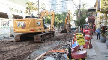 Retroescavadeira operando em rua com cones de interdição em volta. #pracegover