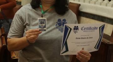 Voluntária exibe crachá e certificado recebidos na Sala Princesa Isabel. #paratodosverem