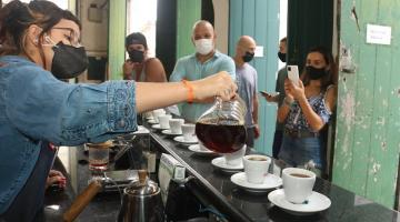 Barista serve café para grupo de turistas, que observam e tiram fotos. #pracegover