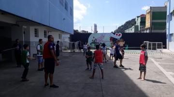 Crianças brincam na quadra da escola. Elas jogam bola com as mãos e usam coletes para diferenciar os times #Pracegover