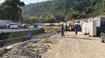 Homens preparam novo trecho de pista para concretagem ao lado de canal. #Pracegover