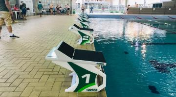 Blocos de partida em padrão específico para competições estão instaladas na beira da piscina. #Pracegover