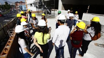 visitantes de capacete estão em círculo na obra #pracegover 