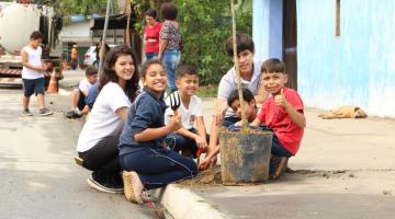 crianças plantando árvore em calçada #pracegover