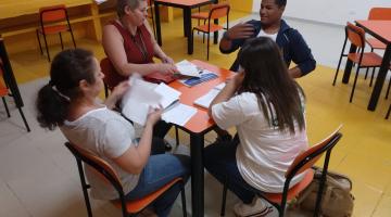 Alunos, representante da Ouvidoria e da equipe escolar estão sentados em torno de uma mesa. #Pracegover