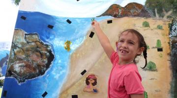 Menina aponta mapa que mostra praia com elementos da natureza