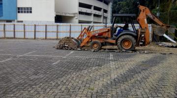 Trator remove piso remanescente de área descoberta. Ao fundo se vê o prédio da Arena Santos. #Pracegover