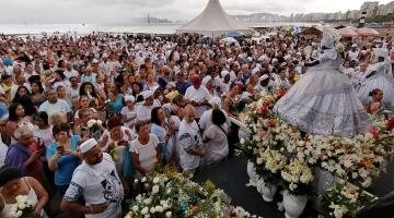 #pracegover na areia da praia, milhares de pessoas observam estátua de Iemanjá exposta sobre patamar