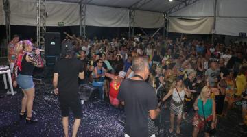 #pracegover Dois homens e uma mulher fazem apresentação mucical no palco, observados por público de cerca de duzentas pessoas dentro de tenda