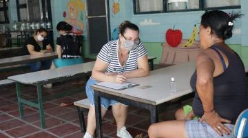 mulheres são atendidas por servidoras de máscara em mesas da escola #paratodosverem 