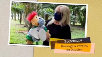 em  trecho do vídeo, professora segura fantoche, ambos de máscara #paratodosverem 