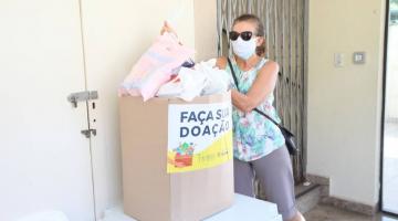 Mulher coloca sacola com doação em uma caixa de papelão #paratodosverem