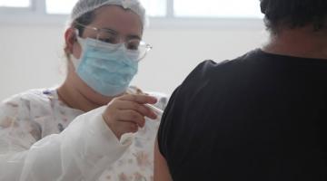 Enfermeira aplica vacina no braço de homem. #paratodosverem