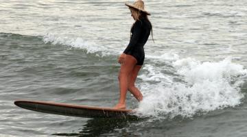 mulher em cima de prancha surfando #paratodosverem