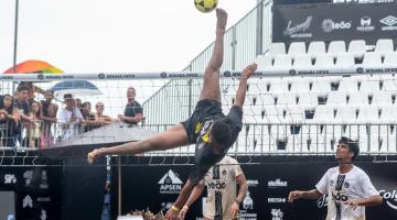 atleta dá salto para chutar a bola em jogo #paratodosverem