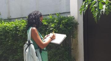 mulher com prancheta na frente de residência #paratodosverem