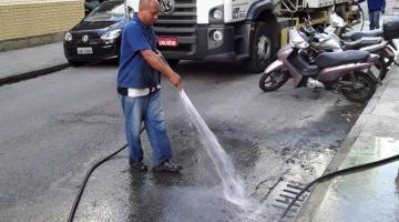 homem segura mangueira que joga água em rua #paratodosverem