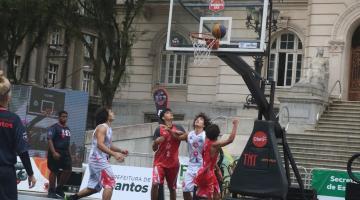 atletas jogam basquete em frente a uma cesta , em praça #paratodosverem