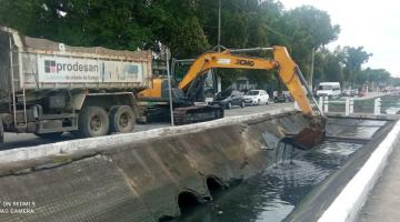 retroescavadeira ao lado de caminhão retira lama de canal #paratodosverem