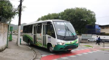 ônibus nas cores verde e branca passando na rua perto de um poste #paratodosverem