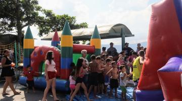 crianças em fila perto de um brinquedo colorido #paratodosverem