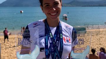 atleta na praia segurando troféus e medalhas #paratodosverem