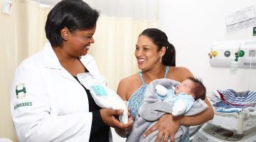 enfermeira sorri para mãe que segura criança no hospital #paratodosverem