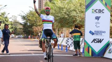 ciclista ergue o braço em comemoração passando a linha de chegada #paratodosverem