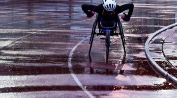 atleta na cadeira de rodas correndo um pista de atletismo molhada #paratodosverem