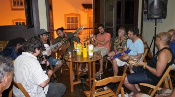 pessoas ao redor de mesa sentadas tocando instrumentos #paratodosverem