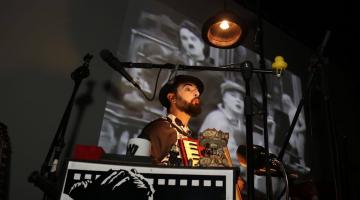 artista tocando no palco com filme sendo exibido ao fundo #paratodosverem