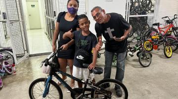 mãe e pai ao lado de filho que segura a bicicleta #paratodosverem