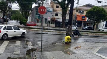 agente usando capa de chuva está junto a bueiro finalizando desobstrução. #paratodosverem