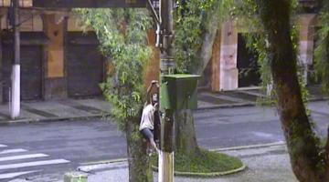 homem está trepado em poste cortando fio de iluminação. #paratodosverem