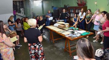 professores estão de pé em uma sala com uma grande mesa com documentos ao centro. #paratodosverem