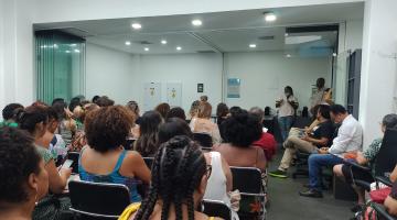 auditório lotado com pessoas sentadas. Ao fundo, um homem faz palestra. #paratodosverem 