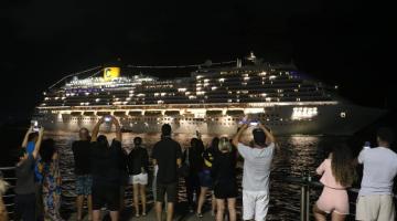 navio saindo à noite e público assistindo em terra. #paratodosverem