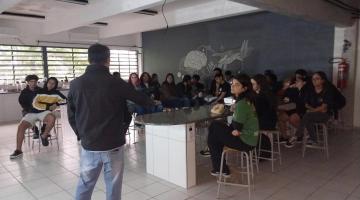 homem de costas fala a estudantes em sala de aula. #paratodosverem