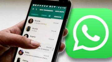 Imagem em close mostra uma mão segurando um smartphone aberto no aplicativo Whatsapp. Ao fundo, o logotipo do whatsapp. #Pracegover