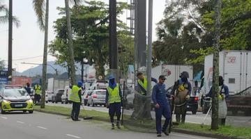 homens uniformizados trabalham na manutenção de canteiro em rua. #paratodosverem