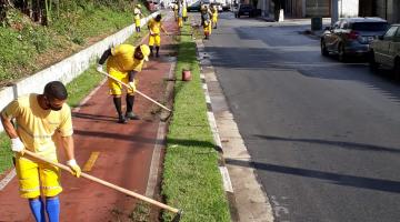 Trabalhando realizam serviço de capinação em canteiro ao lado de ciclovia. #paratodosverem