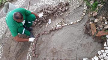 Homem coloca pedras no mosaico da calçada #paratodosverem
