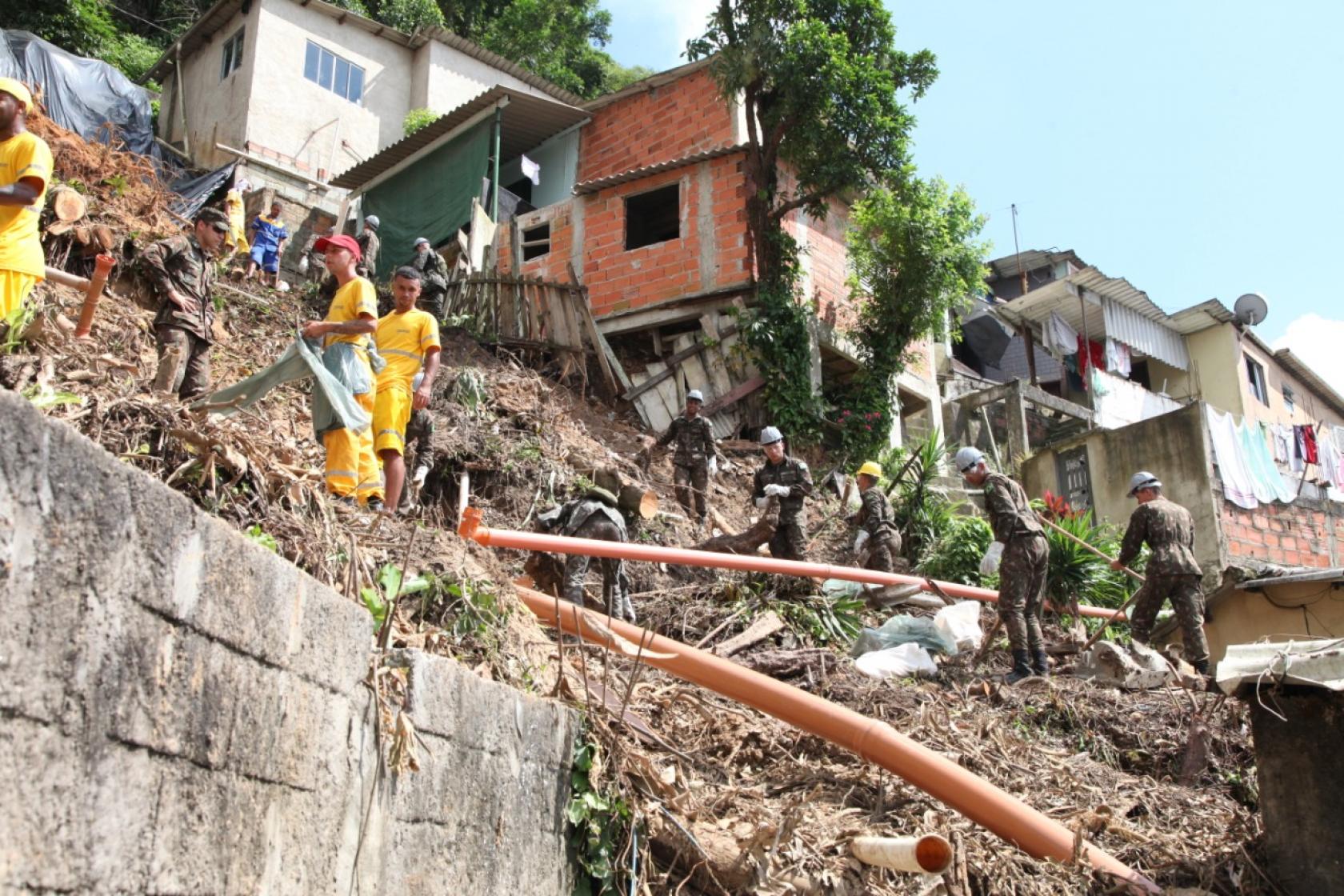 Equipes da Terracom e soldados do Exército no alto de uma encosta fazendo limpeza. #Paratodosverem