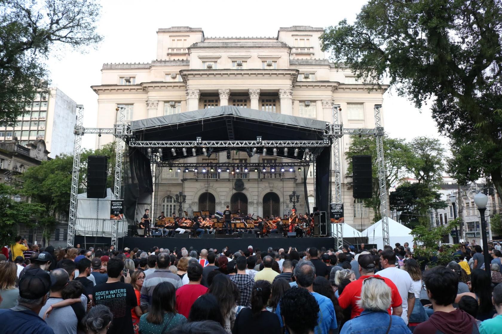 Público está na praça Mauá, diante do grande palco ao fundo e na frente da Prefeitura. A sinfônica toca. 