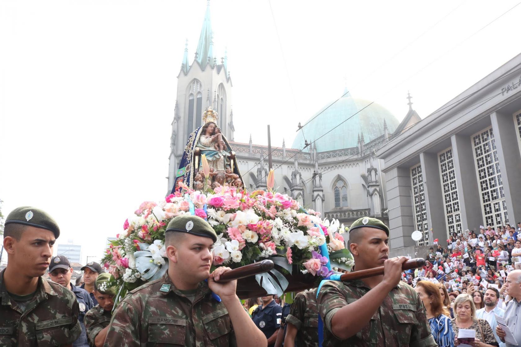 Soldados carregam a santa em andor. Eles passam na frente da Catedral e do fórum. 