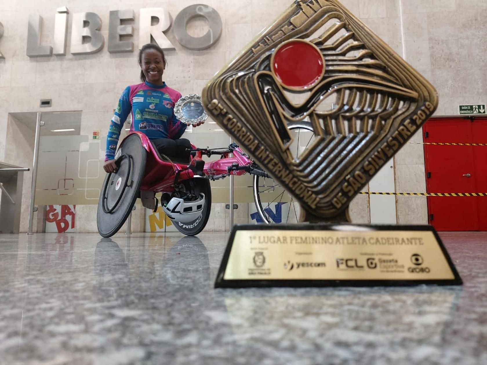 atleta posa na cadeira e troféu está em primeiro plano #pracegover 