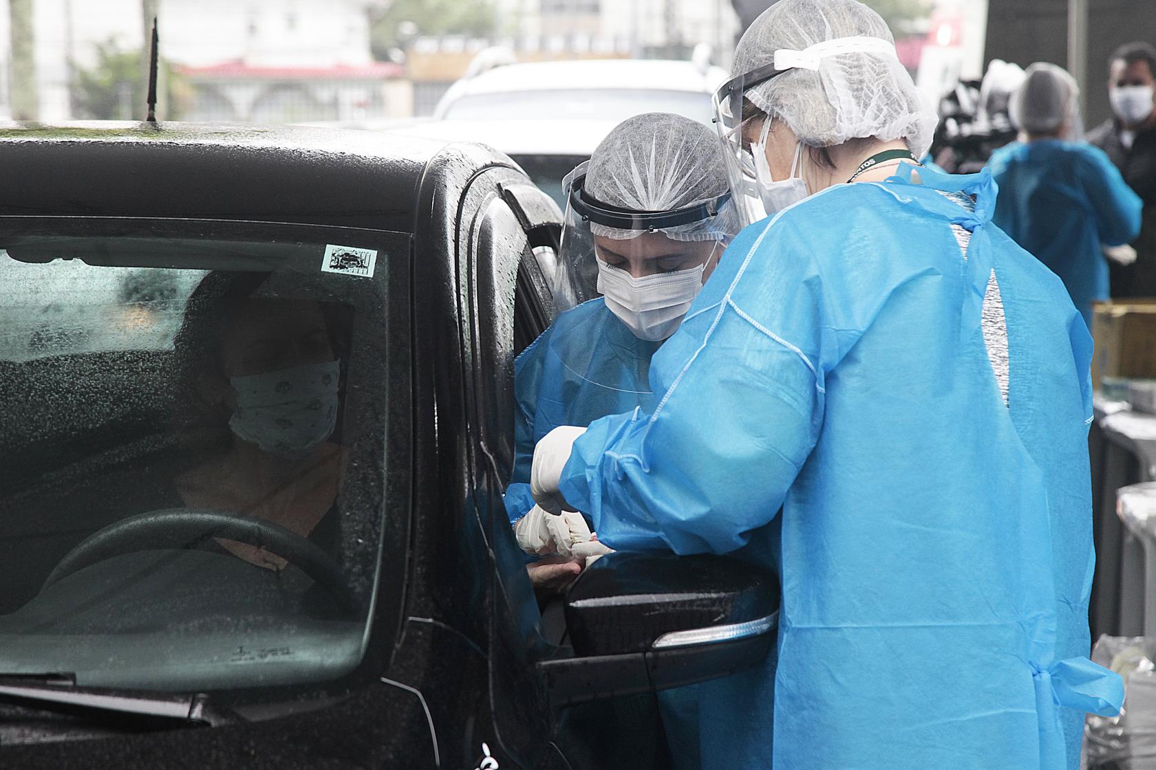 duas técnicas da saúde coletam exame de mulher ao volante de carro #paratodosverem 