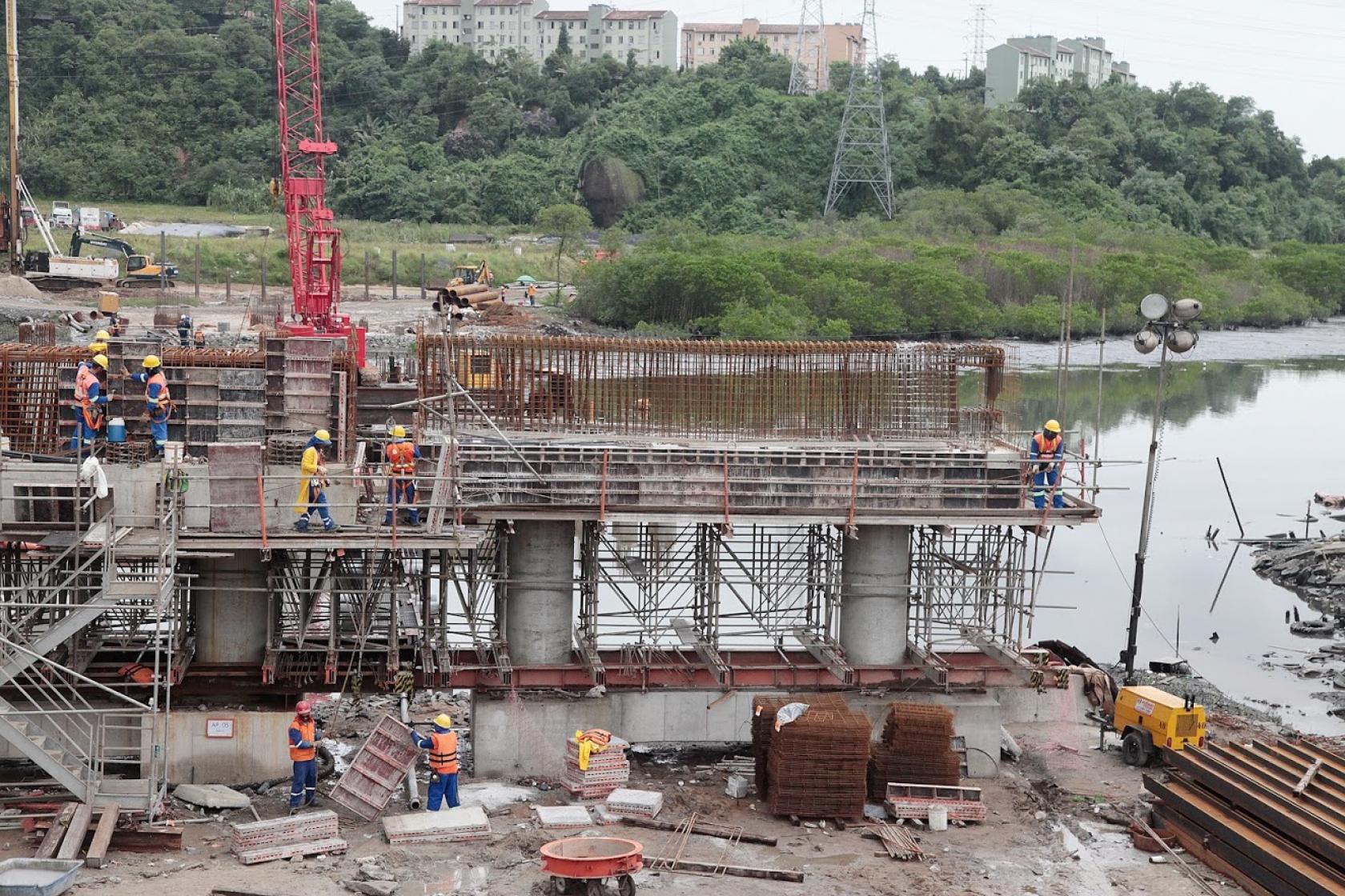 Grande estrutura de ferro rio adentro, com homens trabalhando. #Paratodosverem