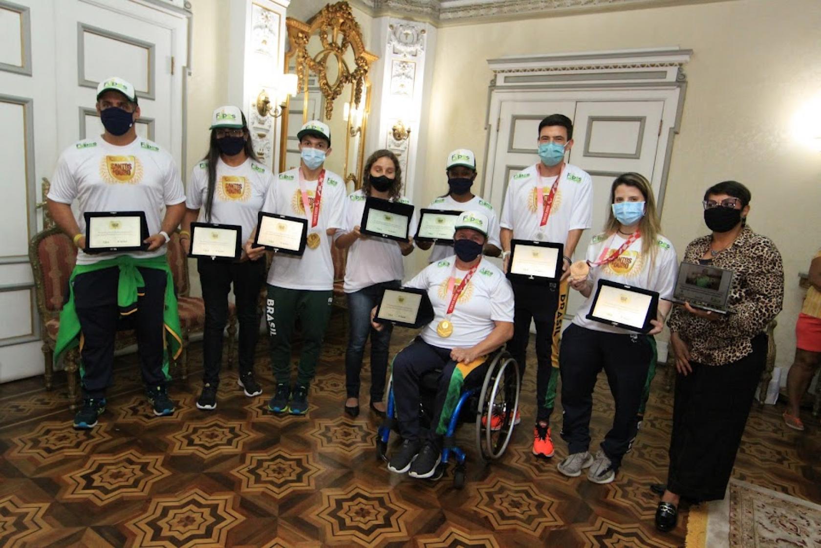 Atletas seguram placas e posam para foto. #paratodosverem